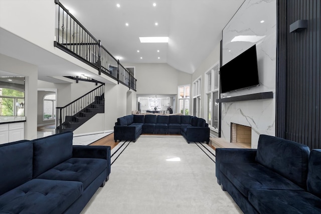 carpeted living room with a fireplace, high vaulted ceiling, and a skylight