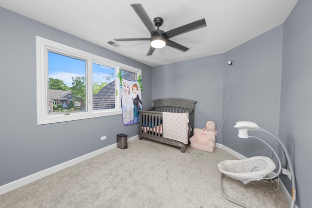 carpeted bedroom featuring ceiling fan and a crib