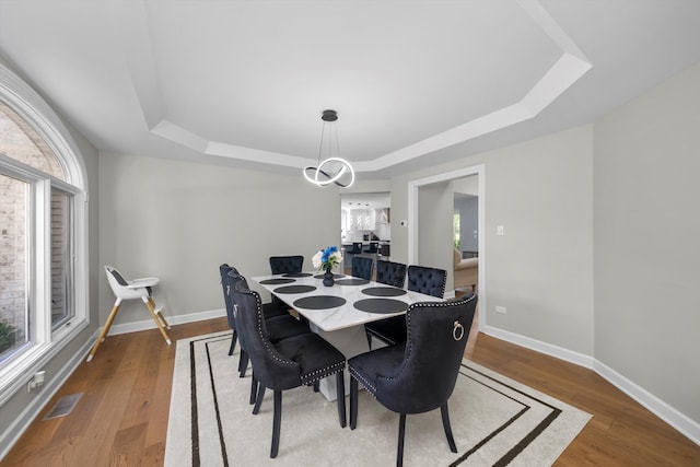 dining area with a raised ceiling and wood-type flooring