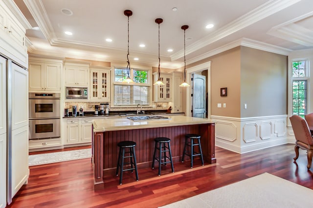 kitchen with hanging light fixtures, a breakfast bar area, appliances with stainless steel finishes, a kitchen island, and dark wood-type flooring