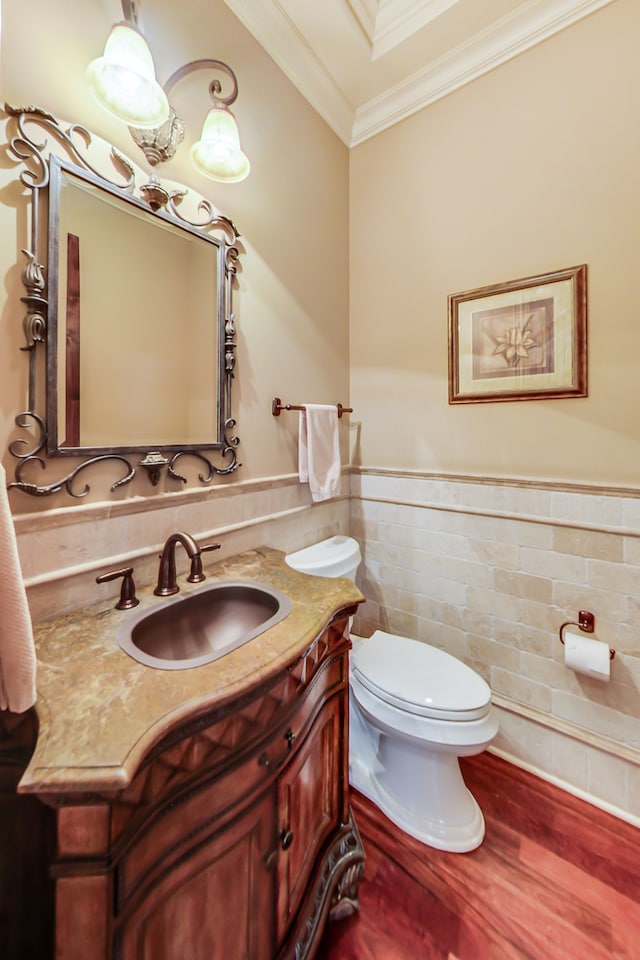 bathroom with wood-type flooring, tile walls, toilet, ornamental molding, and vanity