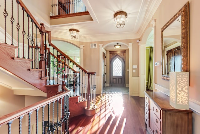 foyer entrance with dark wood-type flooring, ornate columns, ornamental molding, and a chandelier