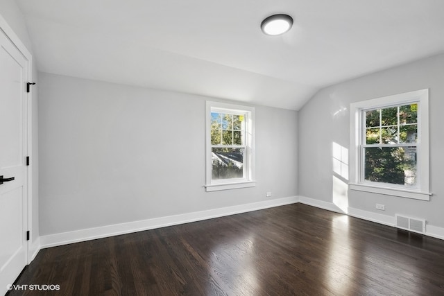 empty room with dark wood-type flooring, vaulted ceiling, and a wealth of natural light