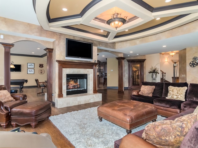 living room featuring coffered ceiling, a tiled fireplace, dark hardwood / wood-style floors, and decorative columns