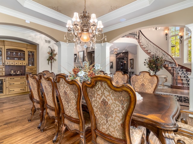 dining area featuring beverage cooler, a raised ceiling, hardwood / wood-style flooring, ornamental molding, and ornate columns