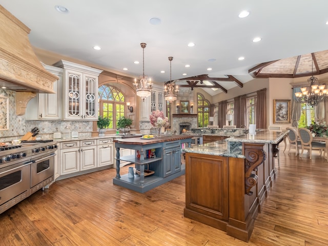 kitchen featuring a kitchen island with sink, hanging light fixtures, lofted ceiling with beams, double oven range, and light hardwood / wood-style floors