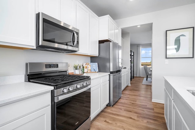 kitchen with appliances with stainless steel finishes, white cabinets, light stone countertops, and light wood-type flooring