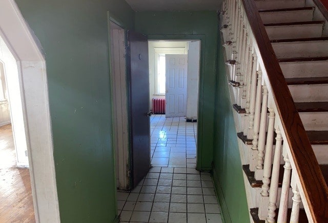 corridor with light tile patterned flooring and radiator heating unit