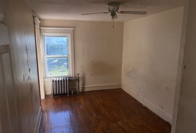 unfurnished room with radiator heating unit, dark wood-type flooring, and ceiling fan