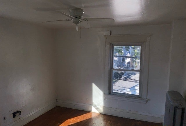 spare room featuring dark hardwood / wood-style floors, radiator, and ceiling fan