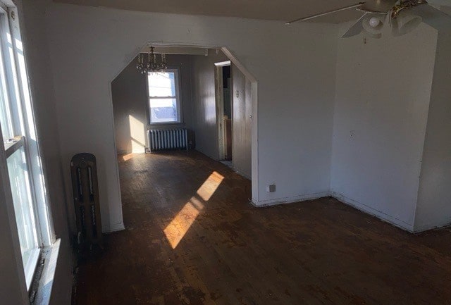 interior space with radiator heating unit, ceiling fan with notable chandelier, and dark hardwood / wood-style flooring