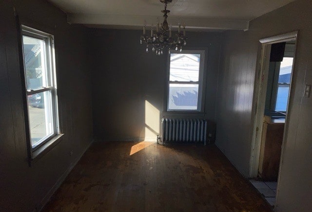 unfurnished dining area featuring an inviting chandelier, hardwood / wood-style flooring, and radiator