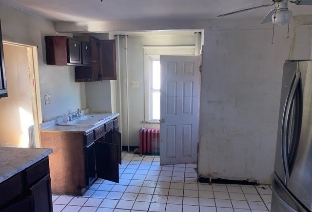 kitchen featuring sink, radiator heating unit, ceiling fan, stainless steel refrigerator, and light tile patterned floors