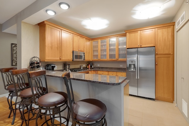 kitchen featuring kitchen peninsula, a breakfast bar, dark stone countertops, and appliances with stainless steel finishes