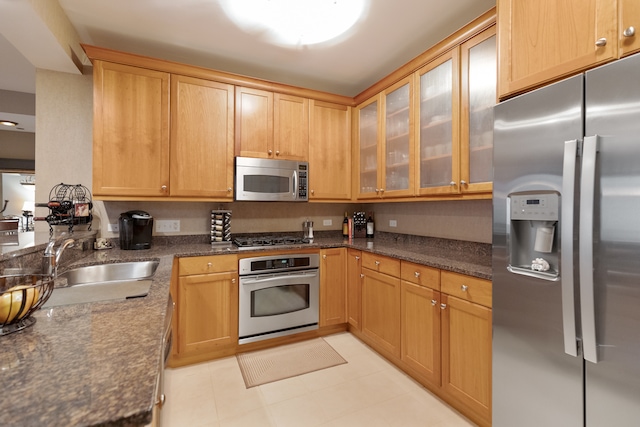 kitchen featuring dark stone countertops, sink, light tile patterned floors, and appliances with stainless steel finishes