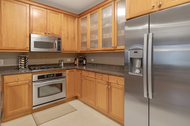 kitchen with light tile patterned flooring, stainless steel appliances, and dark stone counters