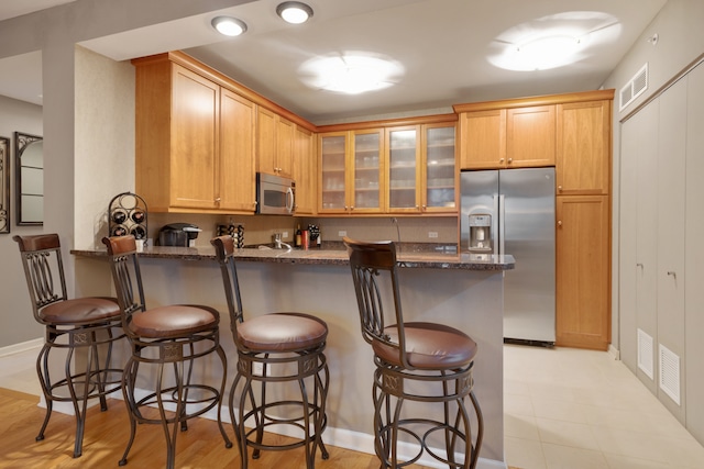 kitchen featuring a kitchen breakfast bar, kitchen peninsula, dark stone countertops, and stainless steel appliances