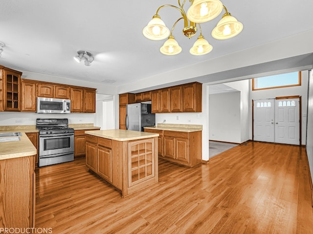 kitchen with sink, light hardwood / wood-style flooring, appliances with stainless steel finishes, decorative light fixtures, and a kitchen island