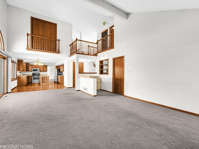 unfurnished living room featuring beamed ceiling, high vaulted ceiling, and light colored carpet