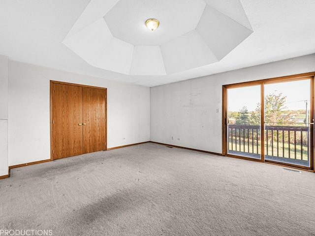 unfurnished bedroom with carpet flooring, a raised ceiling, access to outside, and a closet