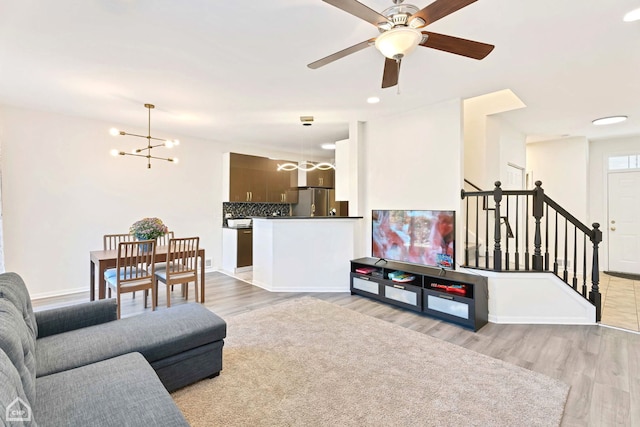 living room featuring ceiling fan with notable chandelier and light wood-type flooring