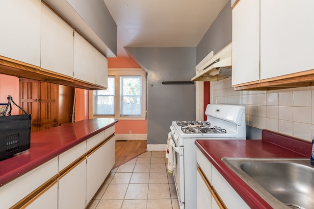 kitchen featuring white gas range, backsplash, white cabinets, light tile patterned flooring, and premium range hood