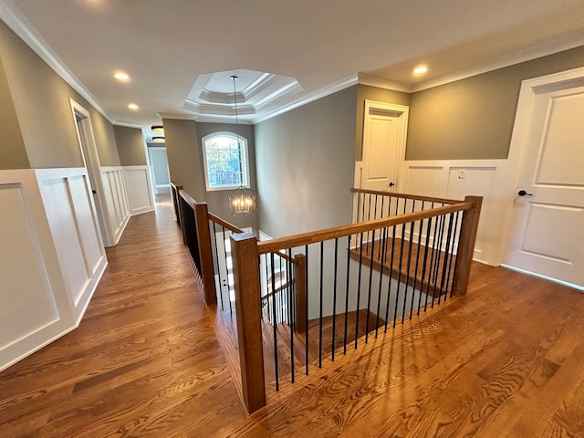 hallway with crown molding, hardwood / wood-style flooring, an inviting chandelier, and a raised ceiling