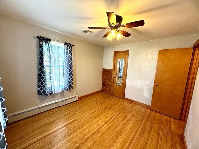 unfurnished bedroom with light hardwood / wood-style flooring, a baseboard heating unit, and ceiling fan