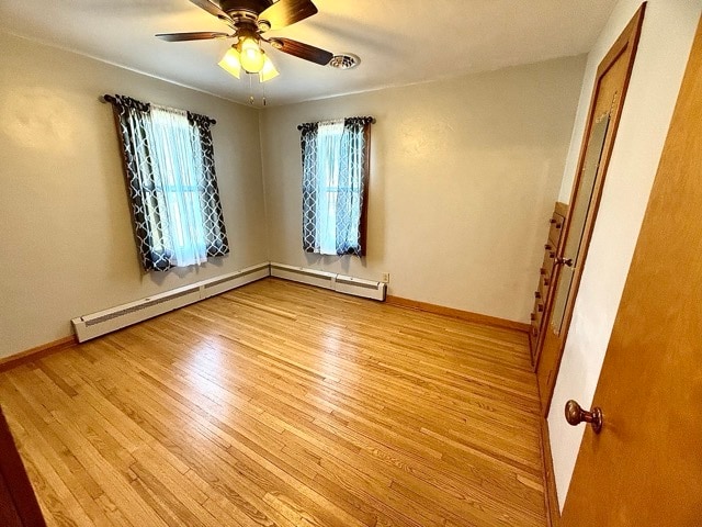 empty room with light hardwood / wood-style floors, a baseboard heating unit, and ceiling fan