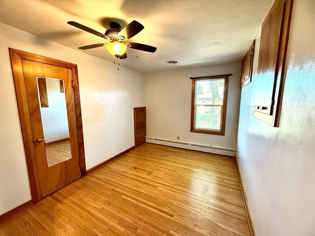 unfurnished bedroom with light hardwood / wood-style flooring, a baseboard heating unit, and ceiling fan