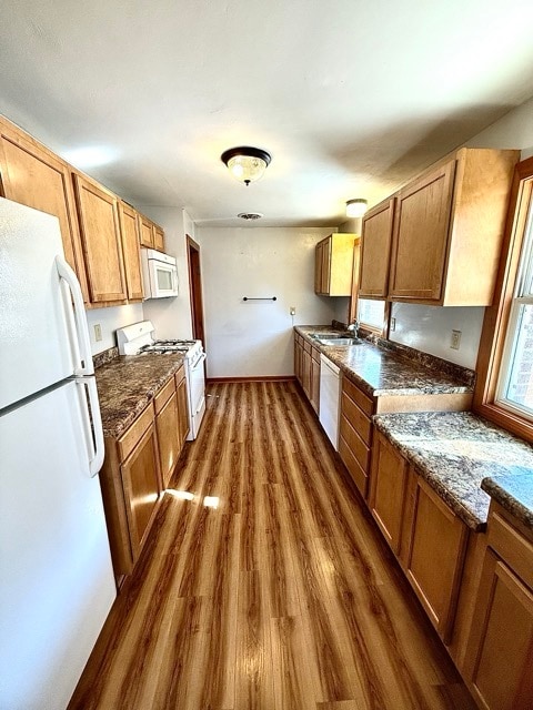 kitchen featuring white appliances, dark hardwood / wood-style flooring, dark stone counters, and sink