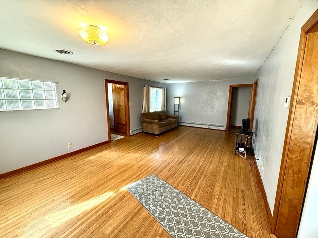 unfurnished living room featuring a baseboard heating unit and wood-type flooring