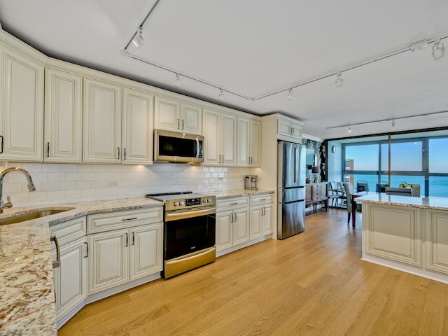 kitchen featuring sink, cream cabinetry, rail lighting, stainless steel appliances, and a water view