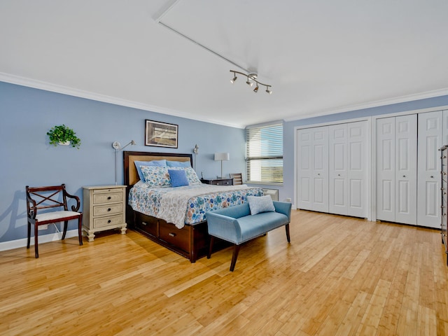 bedroom featuring rail lighting, ornamental molding, light hardwood / wood-style flooring, and two closets