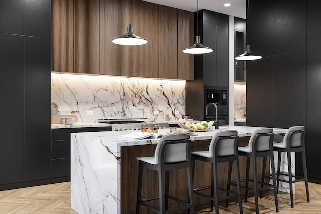 kitchen with light parquet floors, pendant lighting, light stone counters, and an island with sink