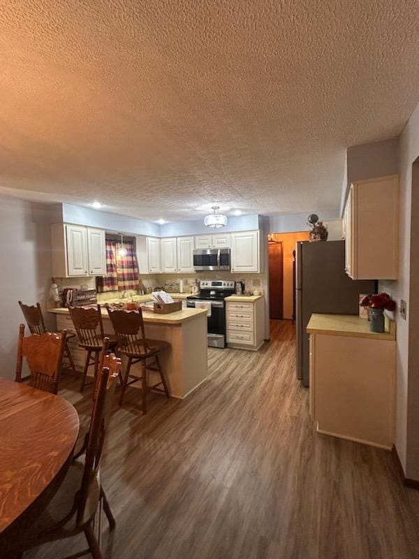 kitchen featuring tasteful backsplash, a textured ceiling, stainless steel appliances, white cabinets, and hardwood / wood-style floors