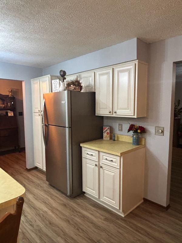 kitchen featuring stainless steel fridge, wood-type flooring, and a textured ceiling