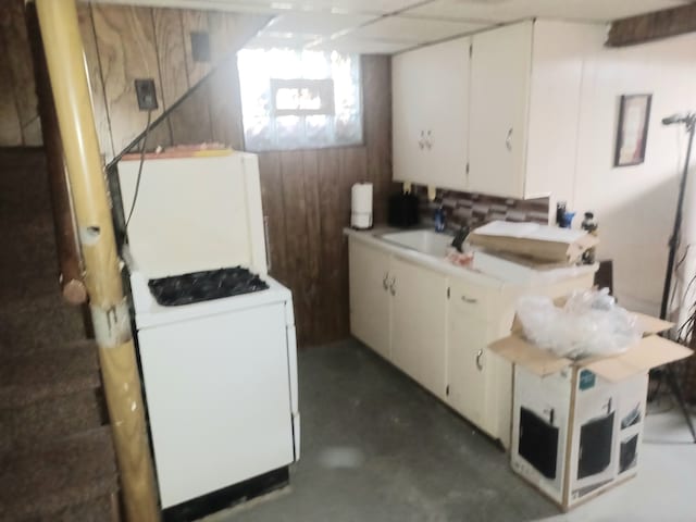 kitchen featuring white cabinets, wooden walls, sink, and white stove