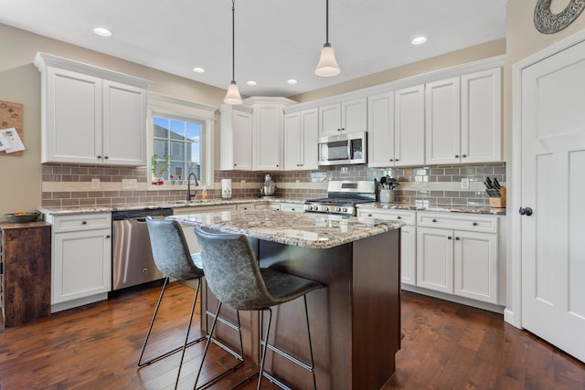 kitchen with a center island, white cabinetry, stainless steel appliances, decorative light fixtures, and dark wood-type flooring