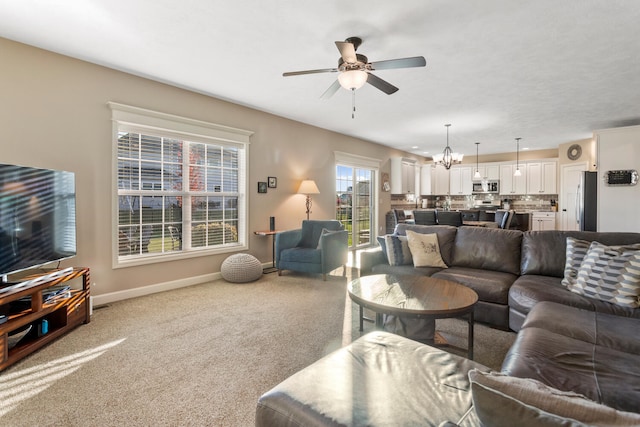 carpeted living room with ceiling fan with notable chandelier