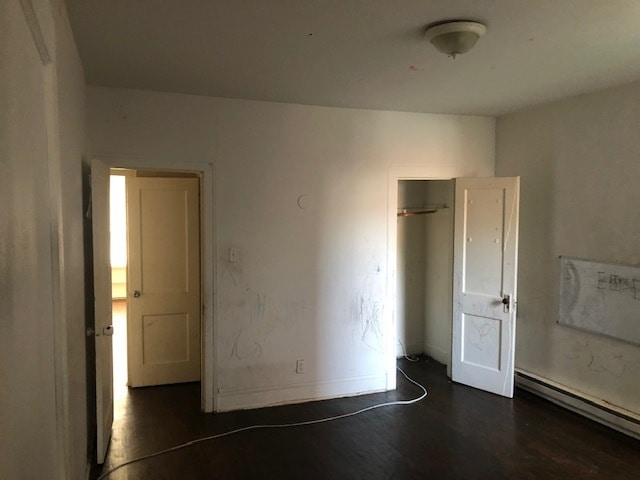 unfurnished bedroom featuring dark wood-type flooring and a baseboard heating unit