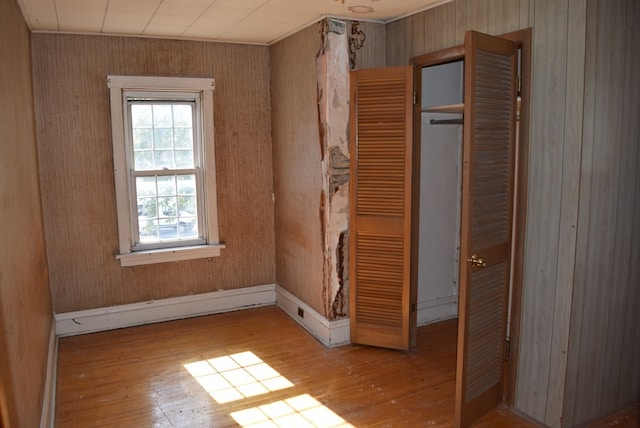 unfurnished bedroom with a closet, light wood-type flooring, and wooden walls