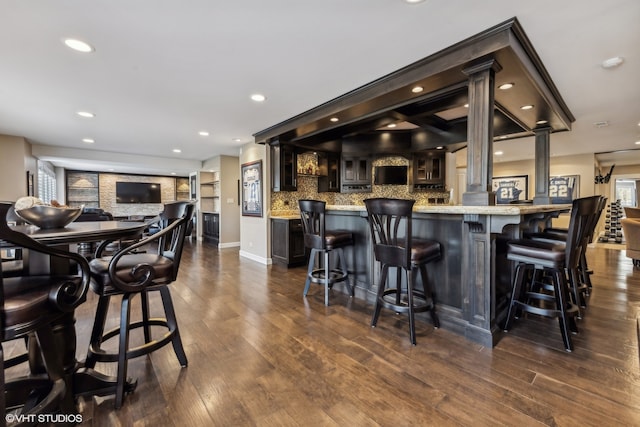 bar featuring dark hardwood / wood-style flooring, decorative columns, dark brown cabinetry, and backsplash