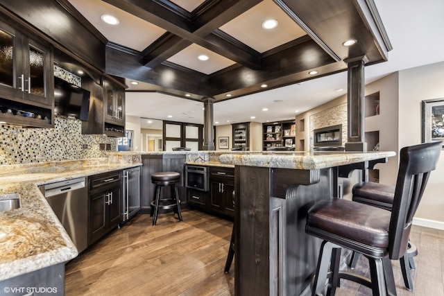 bar featuring hardwood / wood-style flooring, light stone countertops, ornate columns, appliances with stainless steel finishes, and dark brown cabinetry