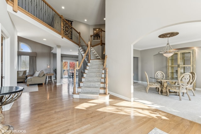 entryway featuring wood-type flooring, ornamental molding, and a towering ceiling