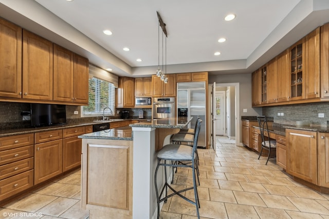 kitchen with a breakfast bar, pendant lighting, built in appliances, dark stone countertops, and a kitchen island