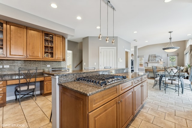 kitchen with stainless steel gas stovetop, backsplash, dark stone counters, decorative light fixtures, and a kitchen island