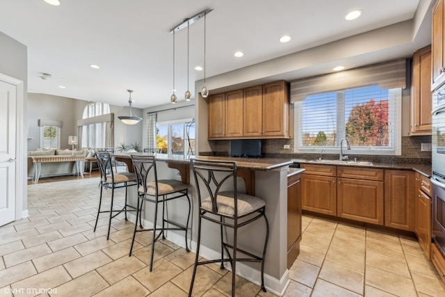 kitchen with a kitchen bar, backsplash, sink, a center island, and hanging light fixtures