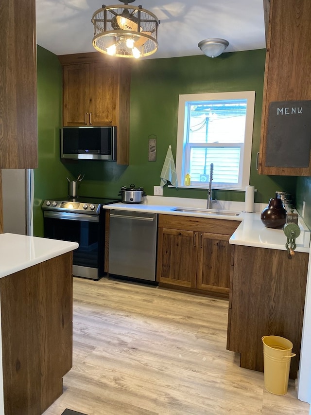 kitchen with appliances with stainless steel finishes, sink, light wood-type flooring, and pendant lighting