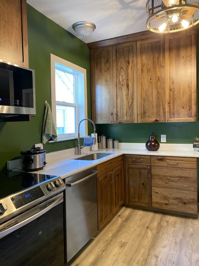 kitchen with appliances with stainless steel finishes, sink, and light wood-type flooring